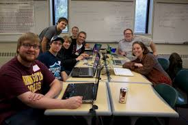 A group of students working together around a desk looking at the camera